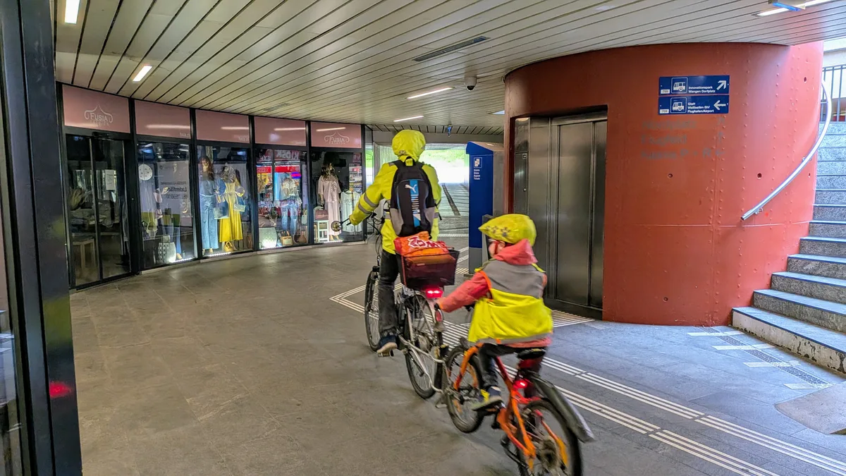 Man sieht eine düstere Bahnhofunterführung mit Passanten und Velofahrern.